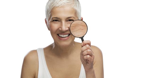 White middle-aged woman with short white hair holding a magnifying glass to her cheek.
