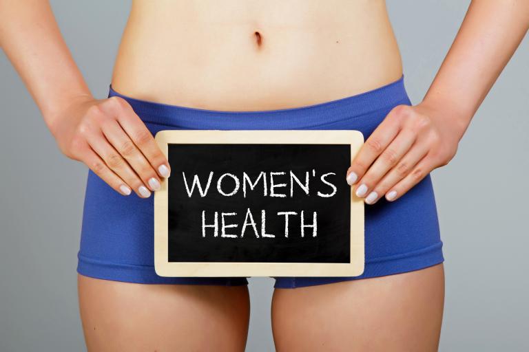 Woman in shorts holding a small blackboard that reads Women's Health.